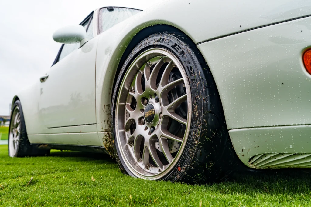 White Porsche 911 wheel and front fender with water droplets on grass