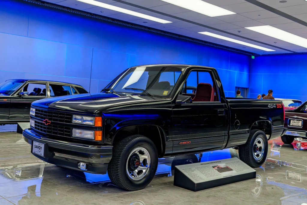 Black Chevrolet 454 SS pickup truck indoors with blue wall and multiple other vehicles visible