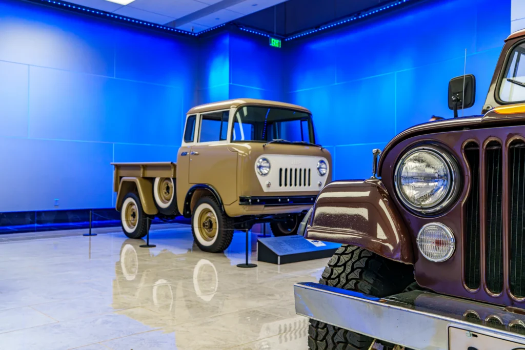 Beige Jeep Forward Control truck shown in profile inside a blue-lit indoor exhibit