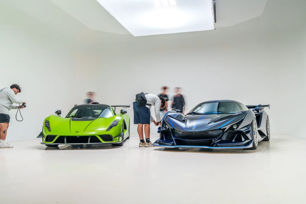 Two high-performance cars, one lime green and one black with blue accents, parked indoors with people around them.