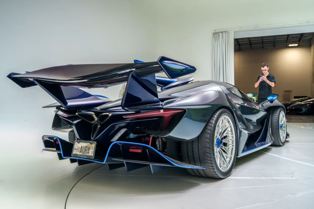 Rear 3/4 view of a dark blue Apollo IE parked indoors near a man using his phone.