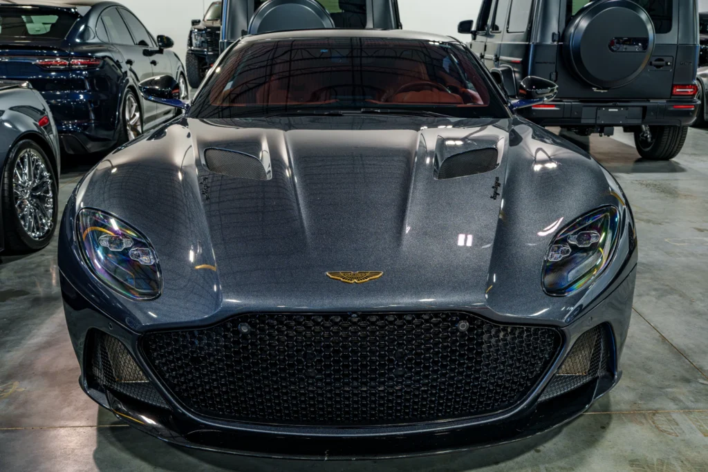 Front view of a dark gray Aston Martin DBS indoors with other vehicles in the background