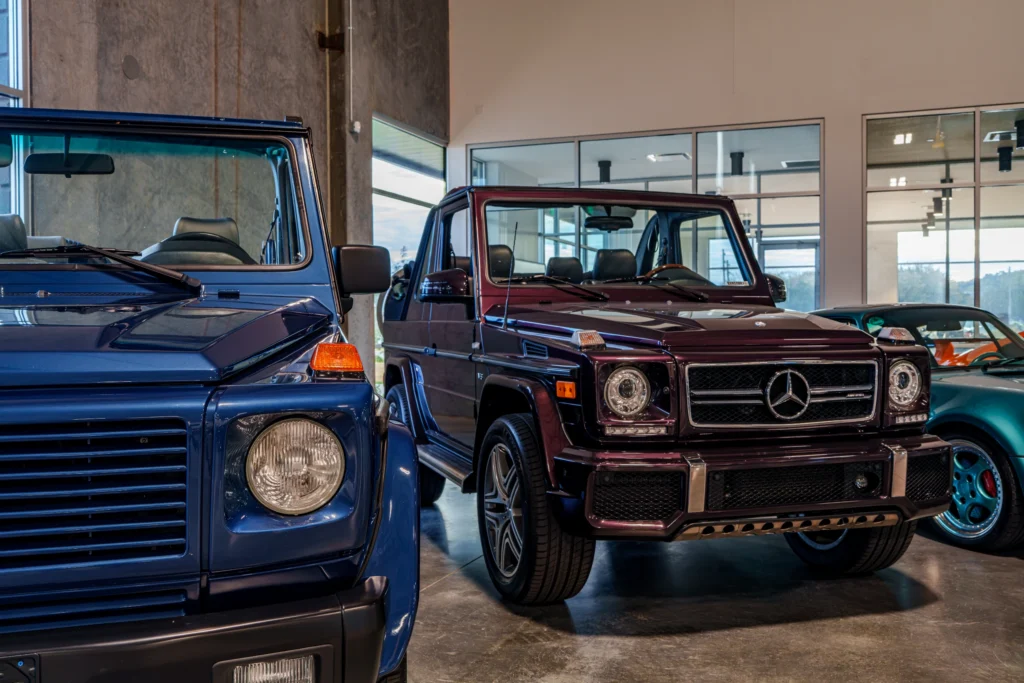 Blue and dark red Mercedes-Benz G-Class Cabriolet indoors near windows with a turquoise car in the background