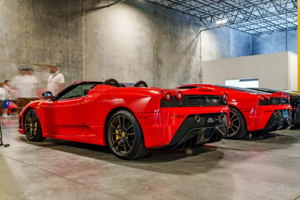 Two red Ferrari F430s, a convertible and a coupe, are displayed side by side inside a hall with attendees nearby.
