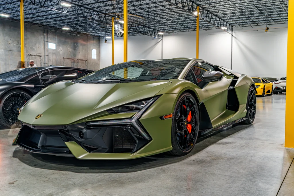 A green Lamborghini Revuelto is parked inside a warehouse with other sports cars.