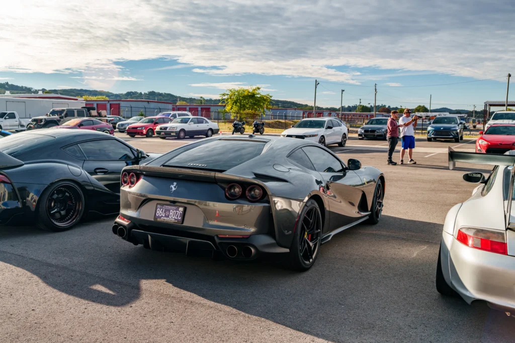 Silver Ferrari 812 Superfast and black Toyota Supra parked in a lot with other vehicles and two people near them