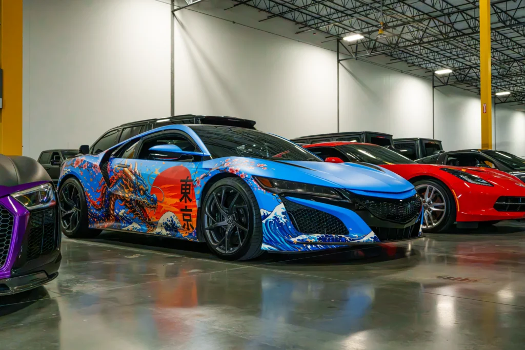 Blue Acura NSX with dragon-themed wrap in an indoor garage with other parked cars