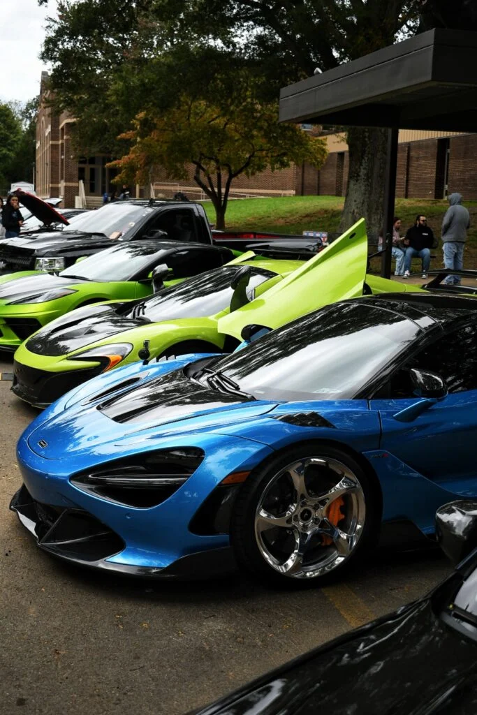 Blue McLaren sports car and two green sports cars parked at an outdoor car event with people in the background