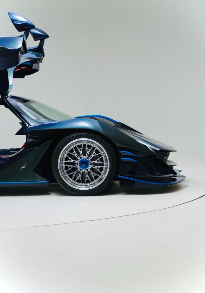 Blue and black Apollo IE rear quarter with open butterfly door and visible wheel on white floor