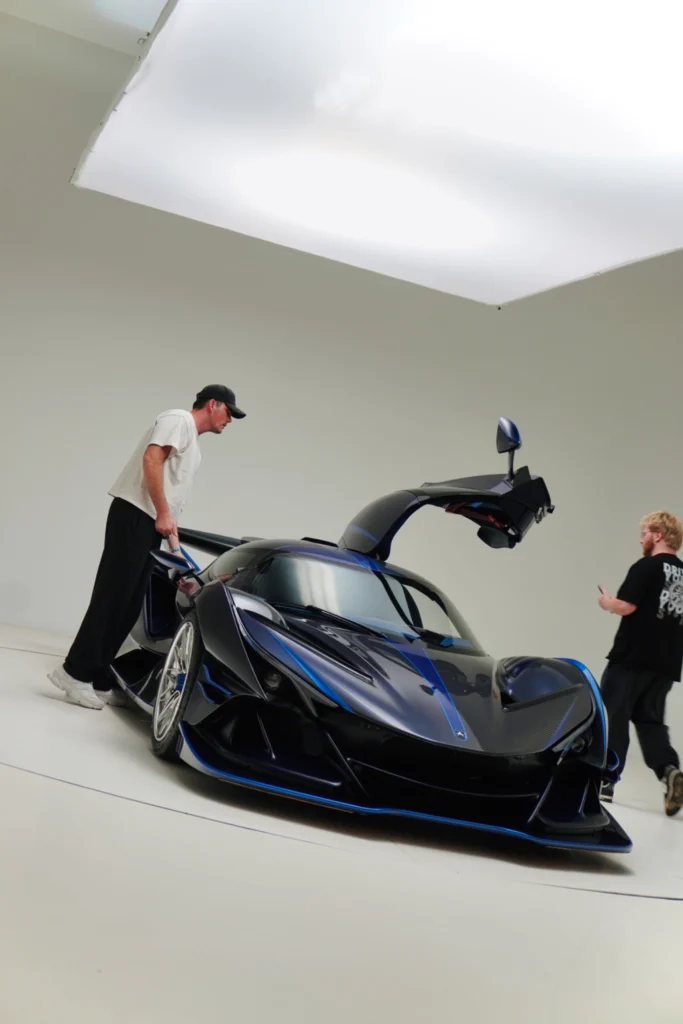 Dark blue Apollo IE with its driver's side door open in a white studio with two men nearby