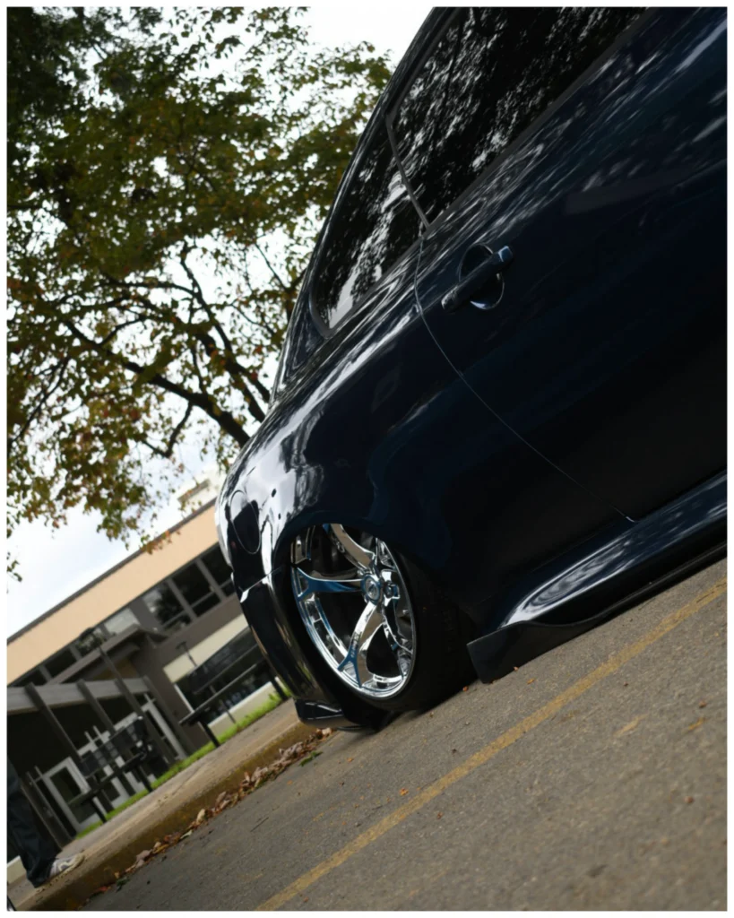 Side view of a dark blue Infiniti G37 with chrome wheels parked outdoors under a tree