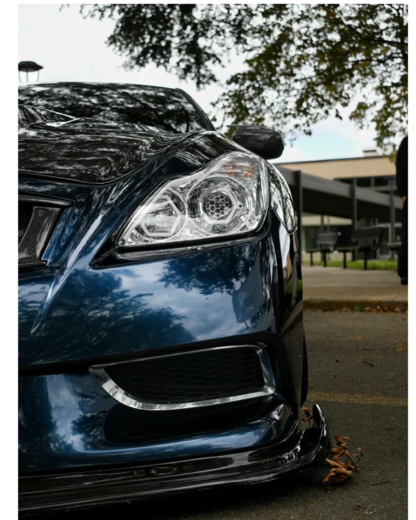Close-up of front left headlight and grille of a Infiniti G37 with reflections of trees and sky