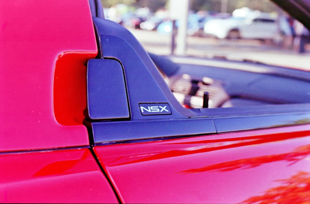 Badge detail of a red Acura NSX showing the NSX emblem near the side window.