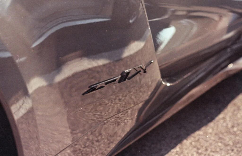 Close-up of black Chevrolet Corvette ZR1X badge on dark surface at an outdoor car event.