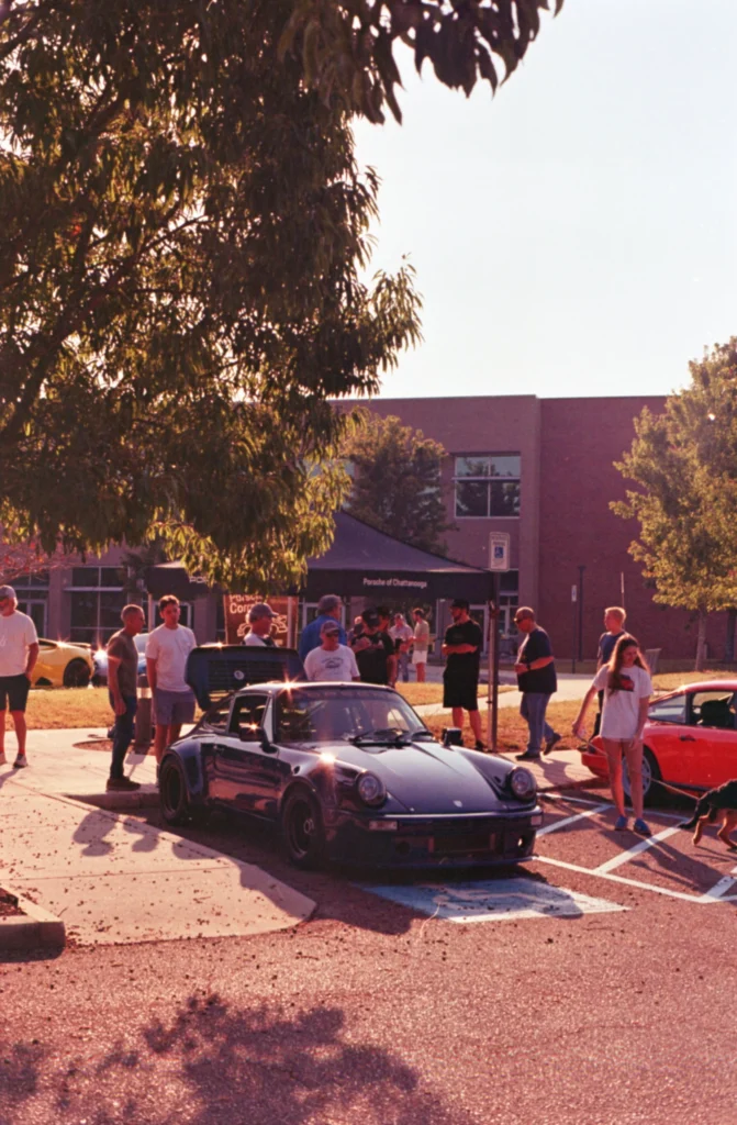 Black Porsche 911 parked at a daytime car event with people and trees in the background