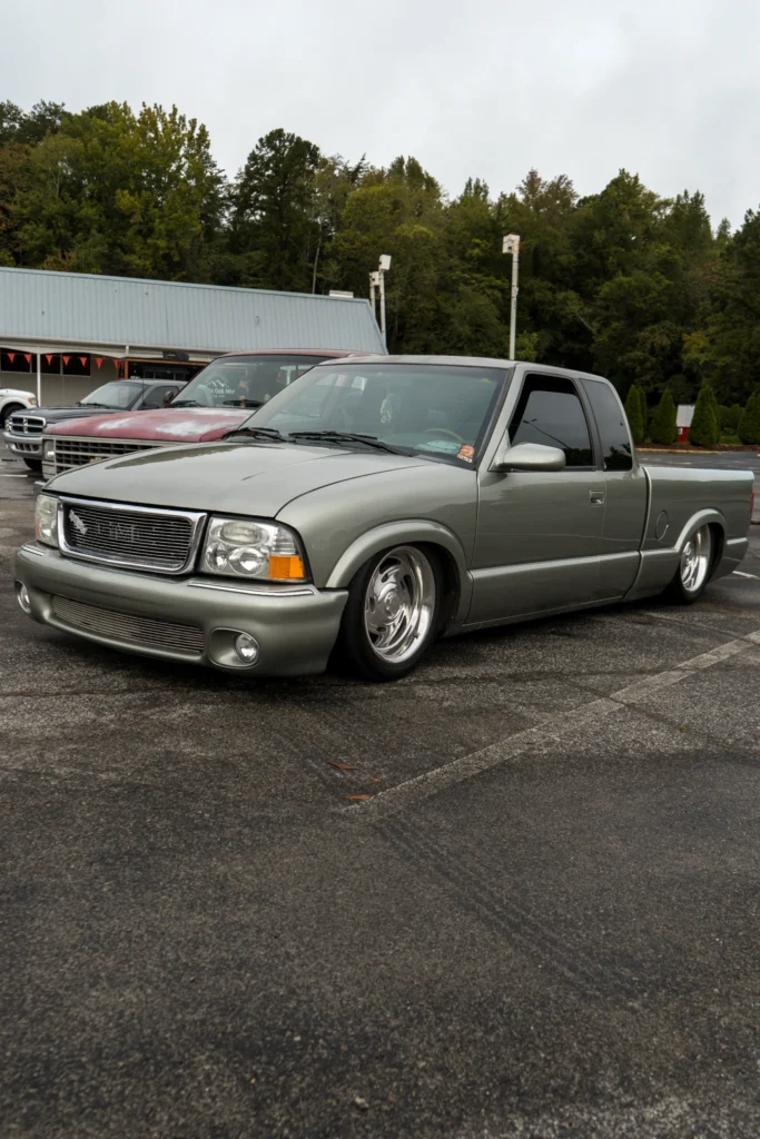 Green GMC Sonoma pickup truck parked at an outdoor event with other vehicles in the background