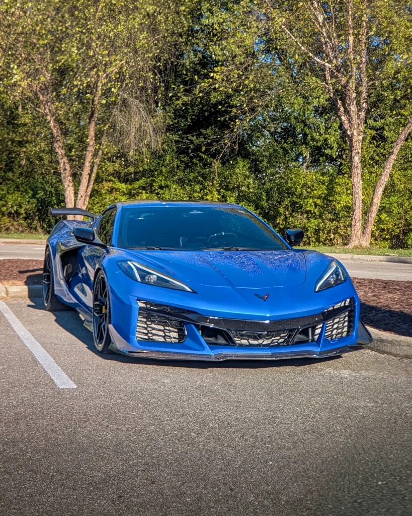 Blue Chevrolet Corvette sports car parked in a lot with trees in the background