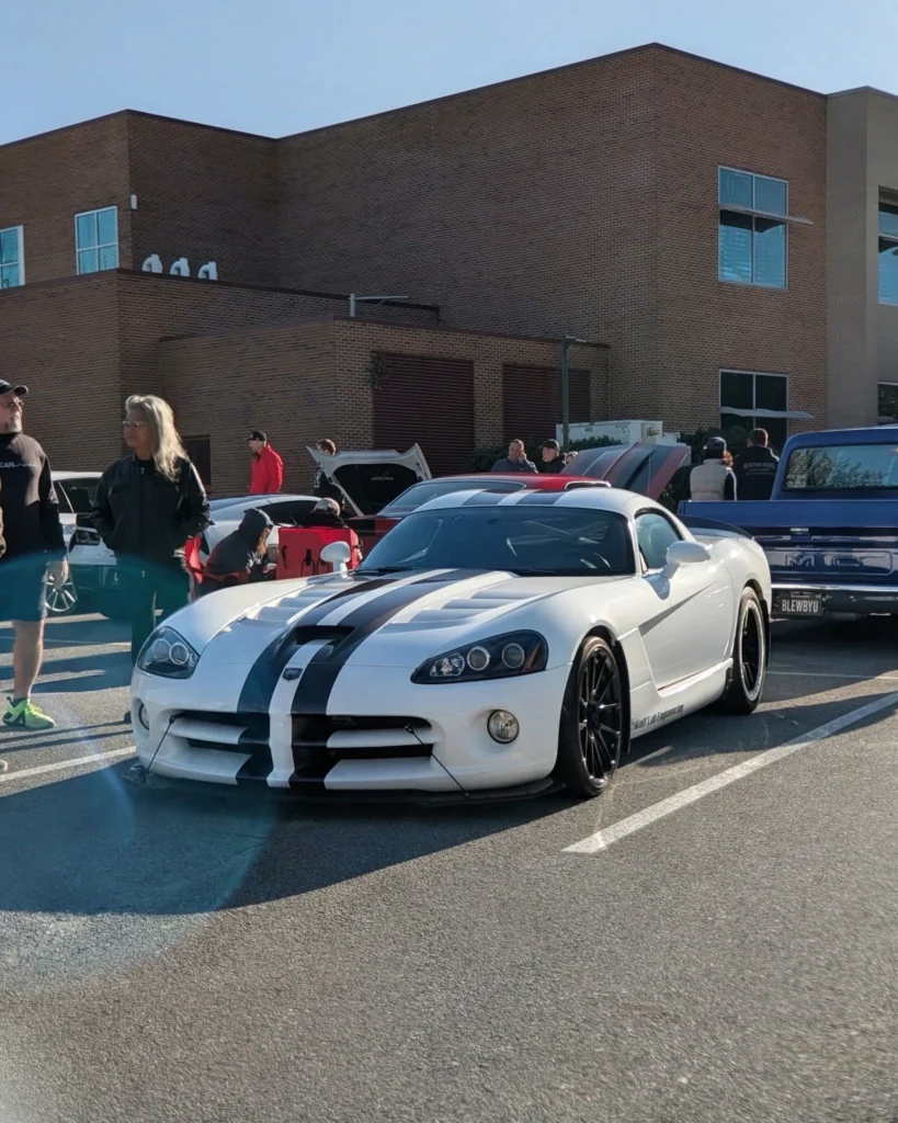 White Dodge Viper with black racing stripes parked at a car event with people and other vehicles nearby