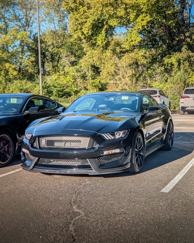Black Ford Mustang Shelby GT350 parked in a lot with trees in the background