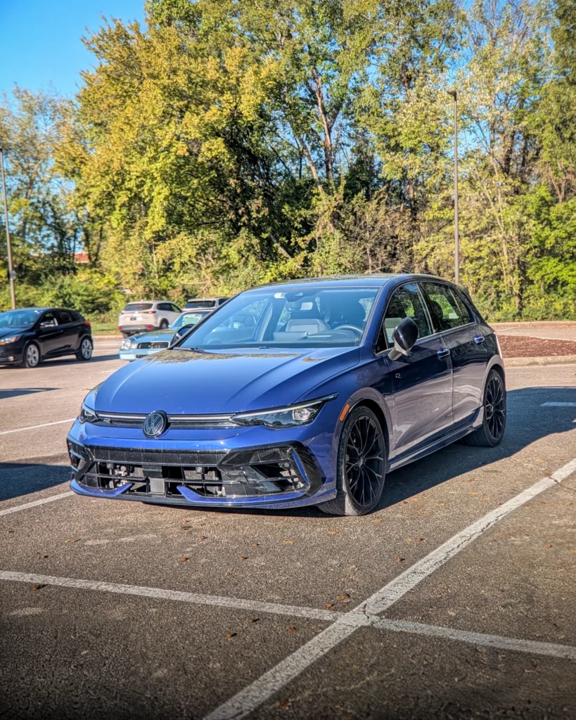 Blue Volkswagen Golf R hatchback parked in a lot with trees and other vehicles in the background