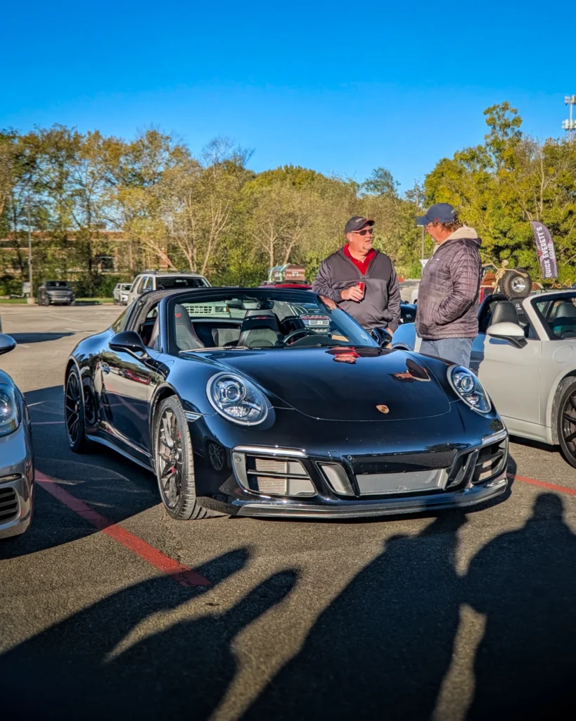 Black Porsche 911 with top down in a parking lot with two men standing beside it talking