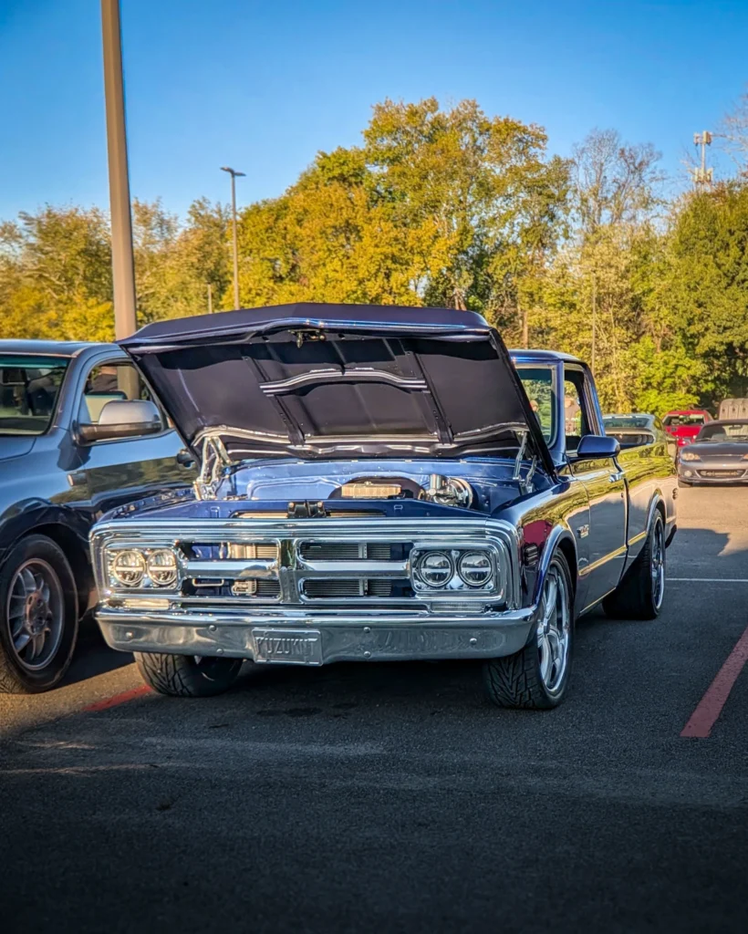 A blue GMC C/K with its hood raised is parked among other vehicles in an outdoor parking lot.