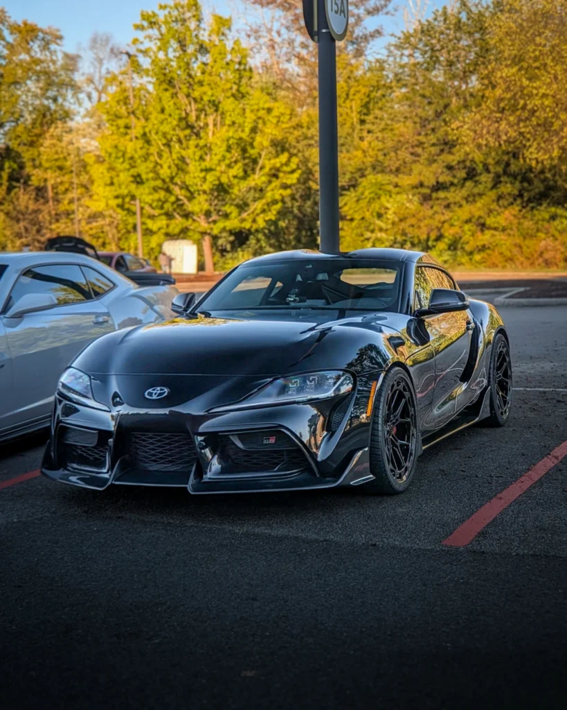 Black Toyota GR Supra parked at an event in late afternoon with trees in background