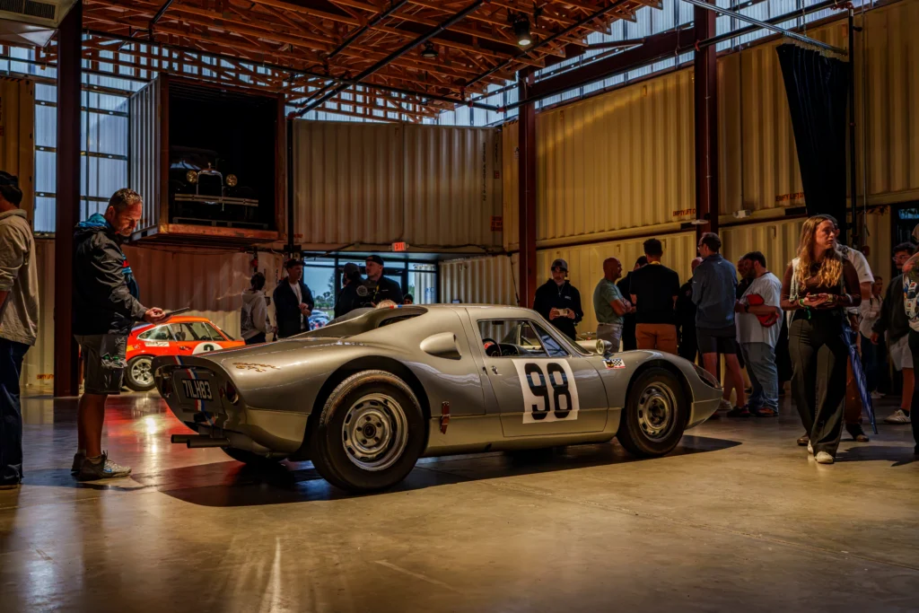 Silver Porsche 904 Carrera GTS race car indoors with people standing nearby at a car event