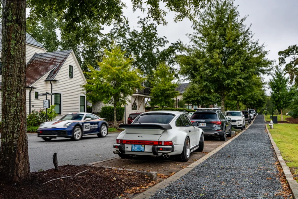 White Porsche 911 Turbo parked on a street with other vehicles and a blue Porsche 911 with racing decals driving past