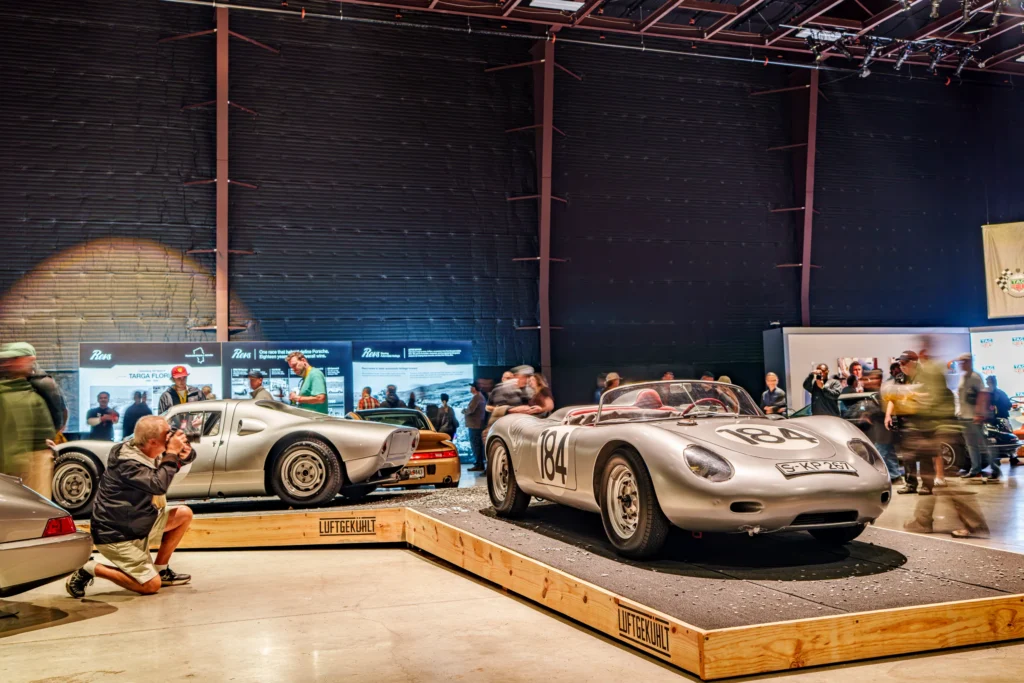 Silver Porsche 550 Spyder race car with number 184 on display indoors alongside a silver Porsche 904 and other cars