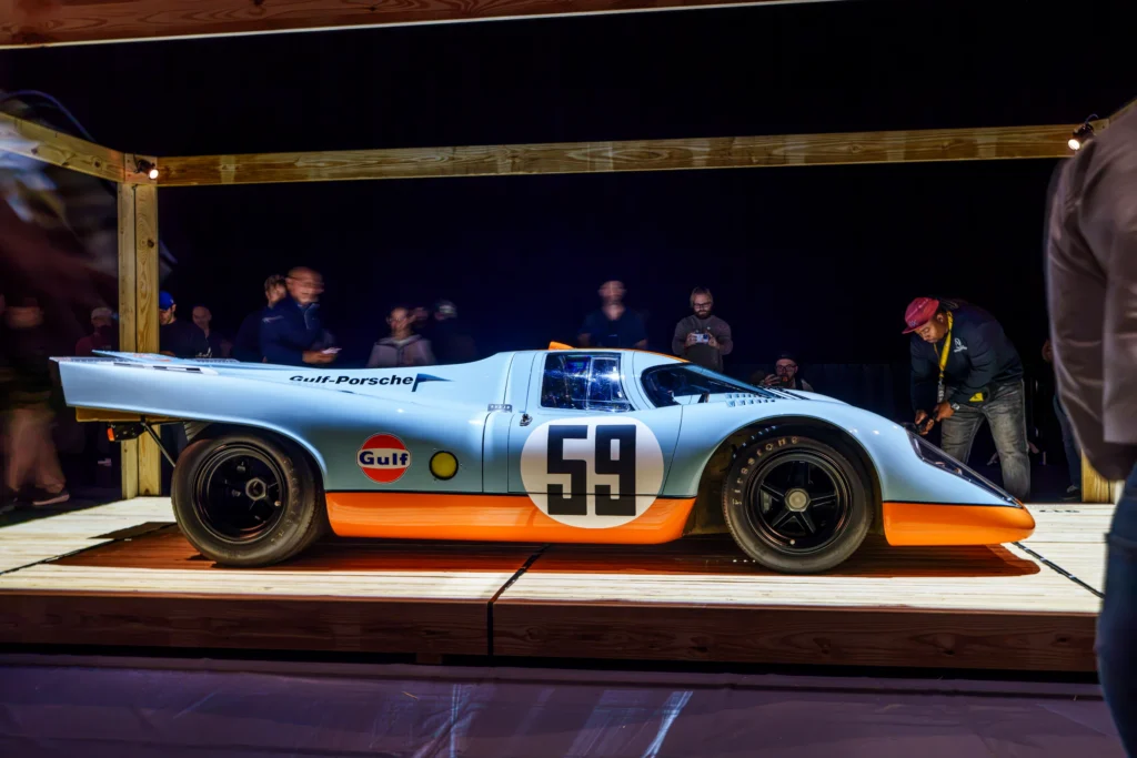 Light blue and orange Gulf-Porsche race car with number 59 on a wooden platform indoors at night
