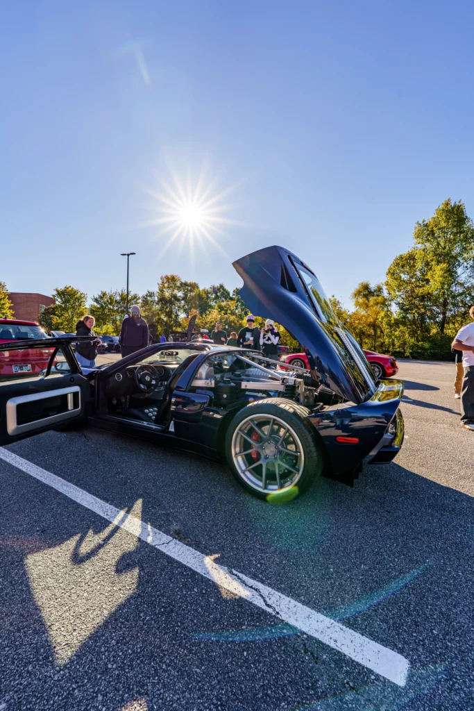 Dark blue Ford GT with open passenger door and raised rear hood showing rear wheels and engine at outdoor car meet