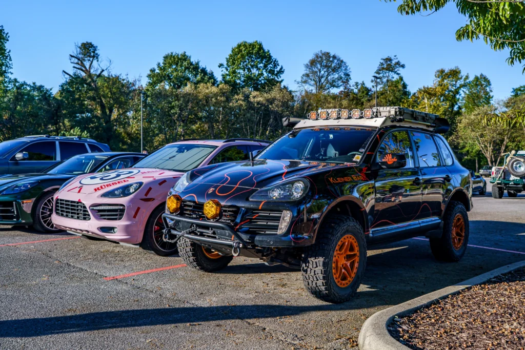 Row of four parked vehicles including a black Porsche Cayenne SUV with off-road modifications and three other SUVs under