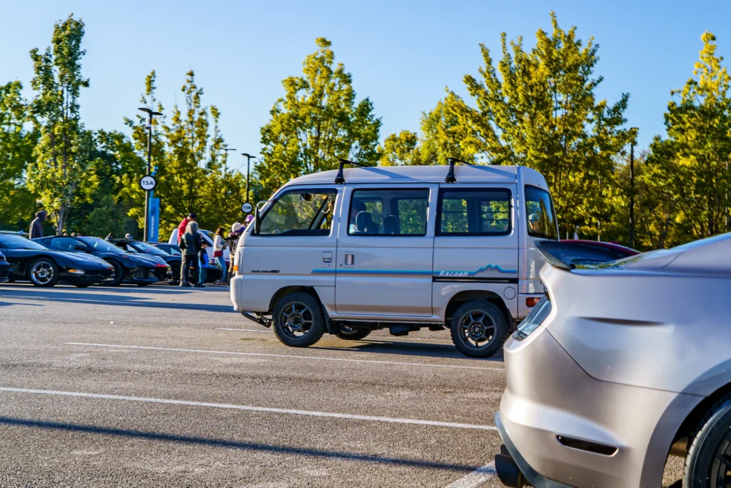 Silver Subaru Impreza hatchbacBeige Suzuki Every van side in parking lot with people and trees in