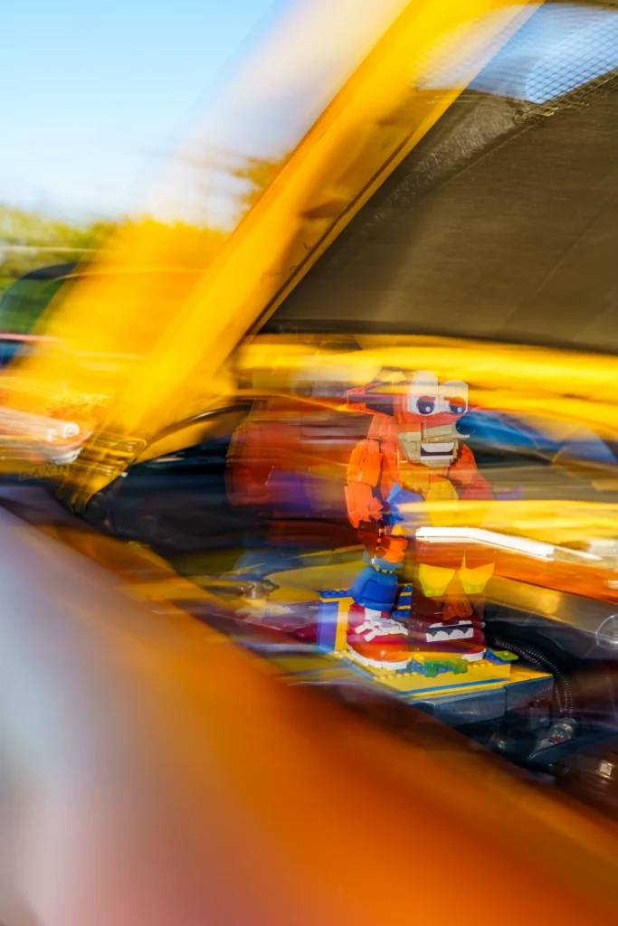 Lego Crash Bandicoot inside a yellow car with motion blur under a clear blue sky