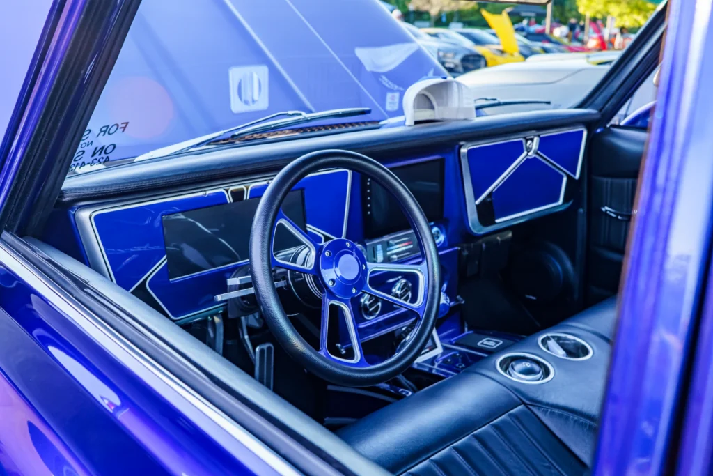 Interior view showing a black and blue steering wheel and dashboard of a purple Chevrolet C10 at a car event