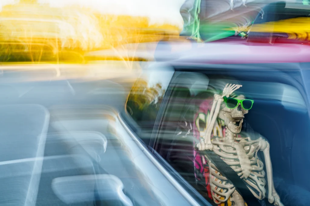 Skeleton wearing green sunglasses seated in a car with motion blur around the vehicle and background
